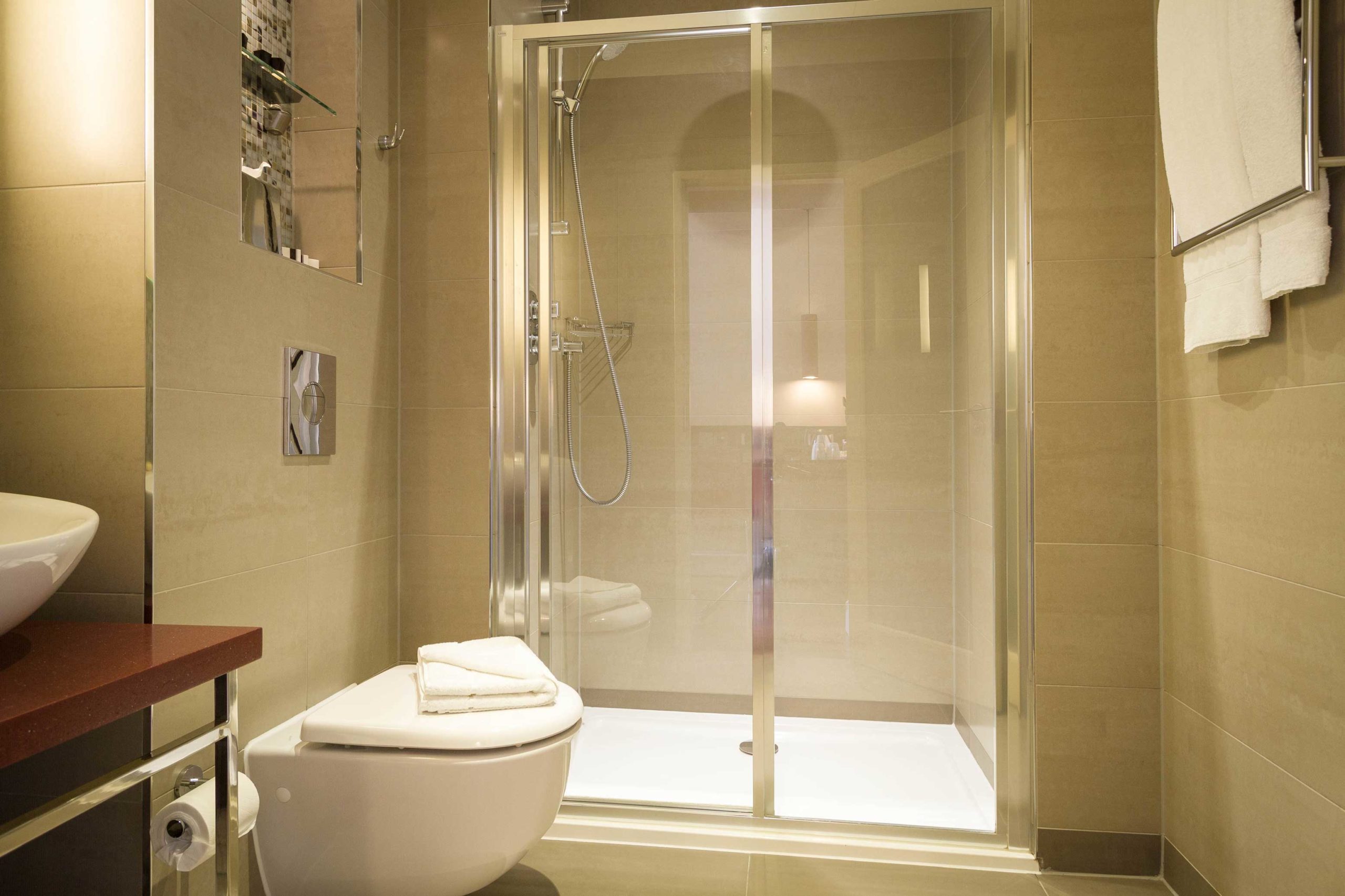 A toilet, shower and towel rack with white towels