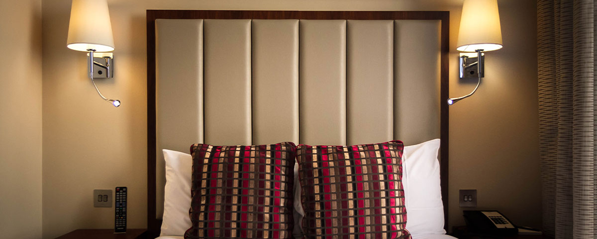 A close up of the red patterned cushions on the bed with two wall mounted lampshades either side.