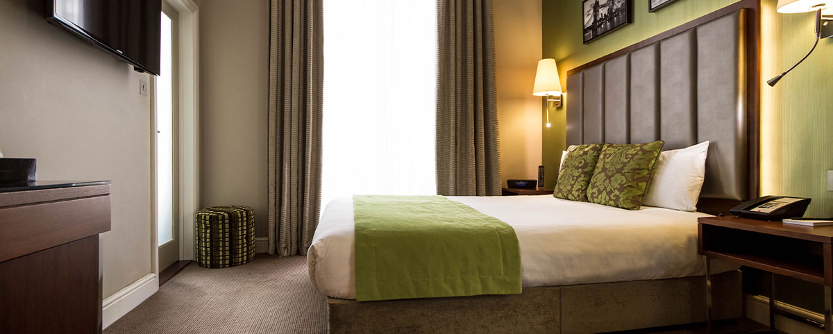 A large bed with a white duvet, green patterned cushions and bed throw.