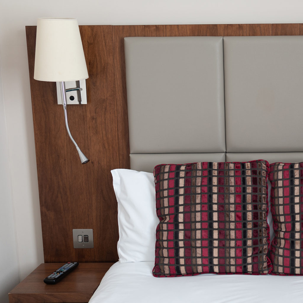 A bed with a white duvet, red patterned cushions